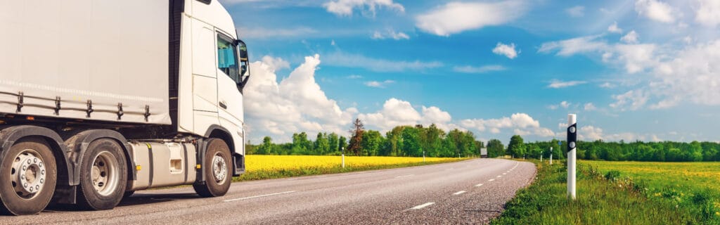 Moving truck on rural road with fields and blue sky in the background.