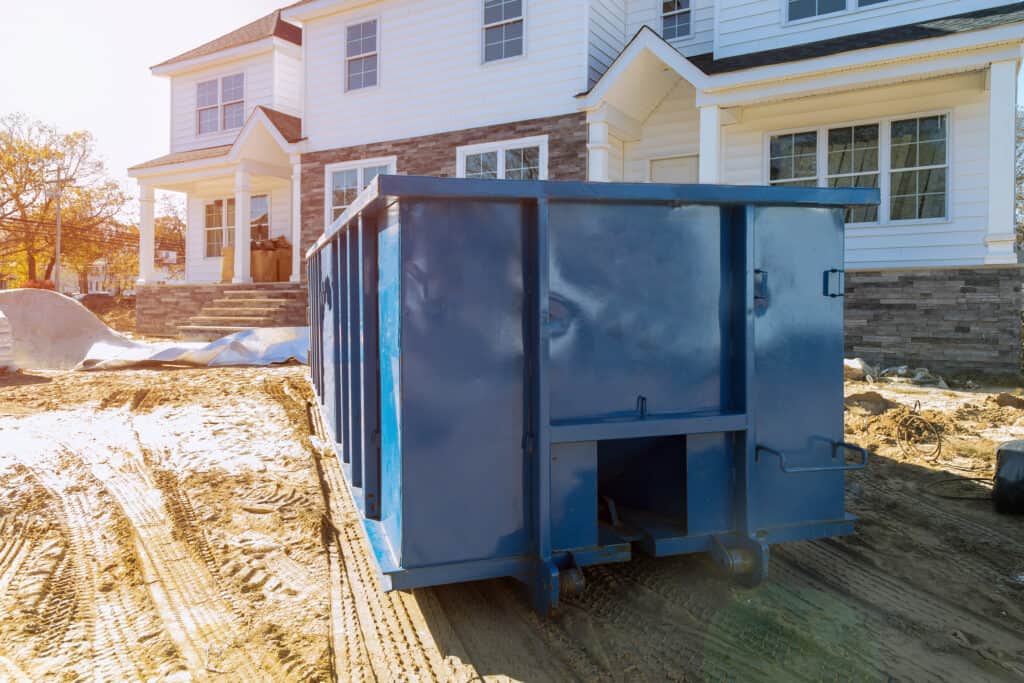 Blue dumpster, recycle waste, and garbage bins near new construction in Long Island, NY.